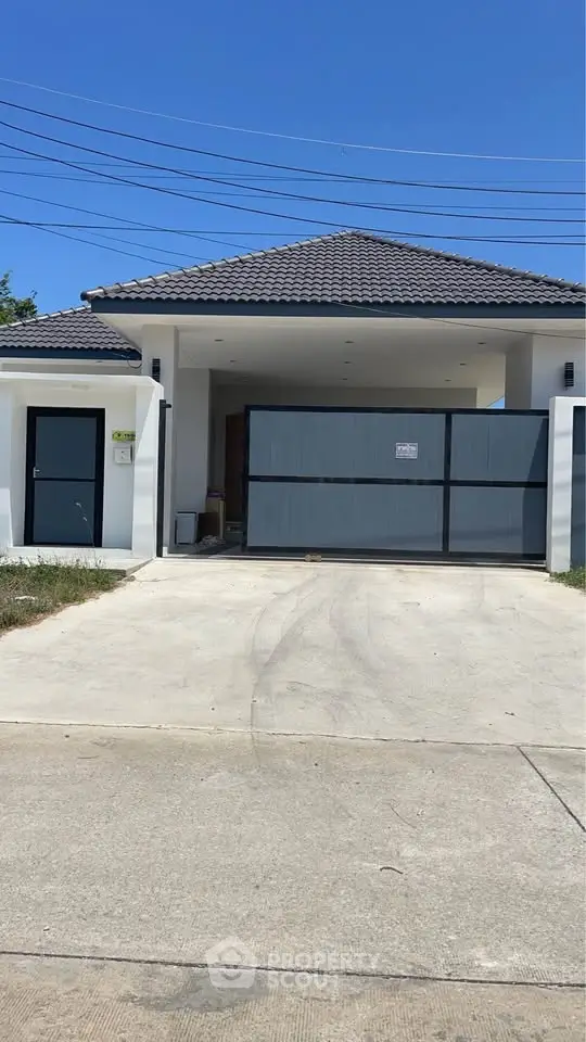 Modern single-story house with gated driveway and tiled roof under clear blue sky.