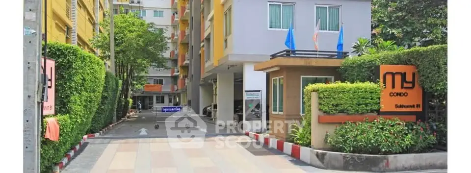 Modern condo entrance with lush greenery and secure gated access in vibrant urban setting.