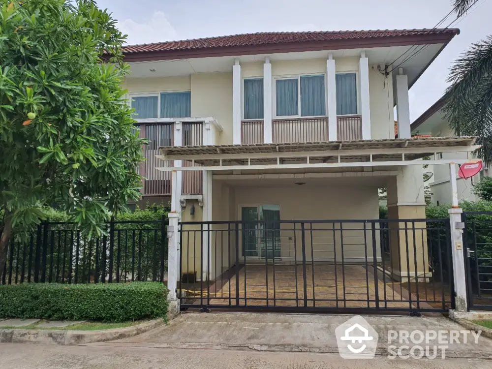 Charming two-story house with gated driveway and lush greenery in a serene neighborhood.