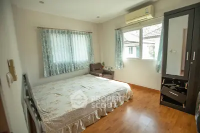 Cozy bedroom with wooden flooring, large window, and air conditioning unit.