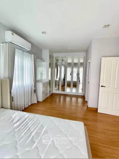 Spacious bedroom with mirrored wardrobe and wooden flooring in modern apartment