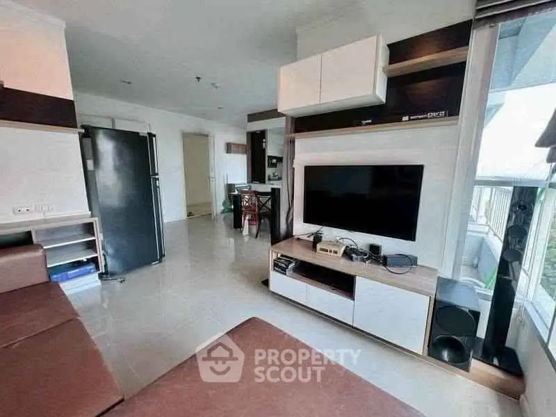 Modern living room with sleek furniture and large TV, open layout leading to dining area, bright natural light.