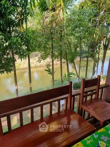 Charming riverside view from a wooden balcony with lush greenery, perfect for relaxation and nature lovers.