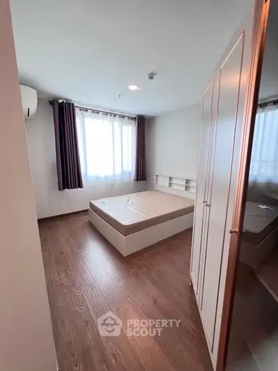 Cozy bedroom with wooden flooring and ample natural light from large window.