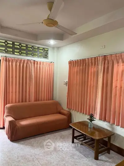 Cozy living room with peach curtains and sofa, featuring a ceiling fan and wooden coffee table.