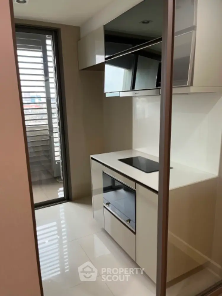 Modern compact kitchen with sleek cabinetry and induction cooktop, adjacent to a balcony with city views.