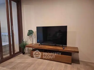 Modern living room with sleek TV stand and large flat-screen TV, adjacent to a balcony with wooden flooring.