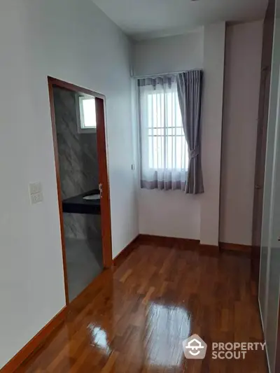 Cozy room with wooden flooring and natural light, adjacent to a modern bathroom.