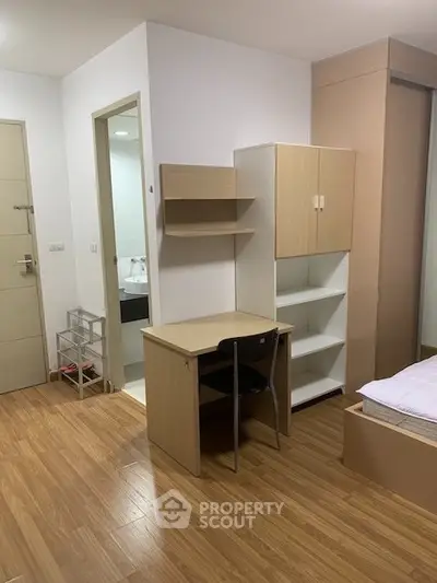 Modern bedroom with wooden flooring, study desk, and built-in storage in a cozy apartment.