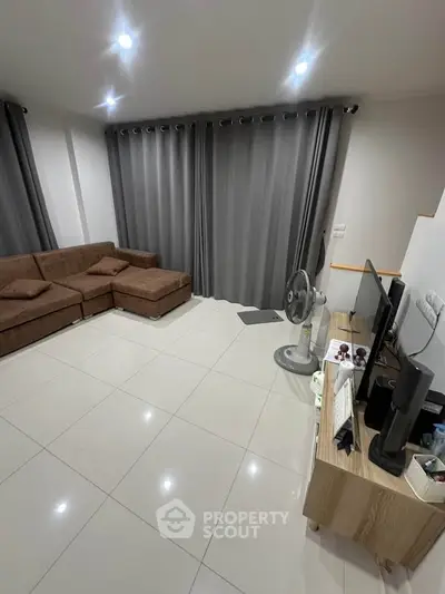 Modern living room with sleek brown sofa and entertainment setup, featuring elegant gray curtains and polished tile flooring.