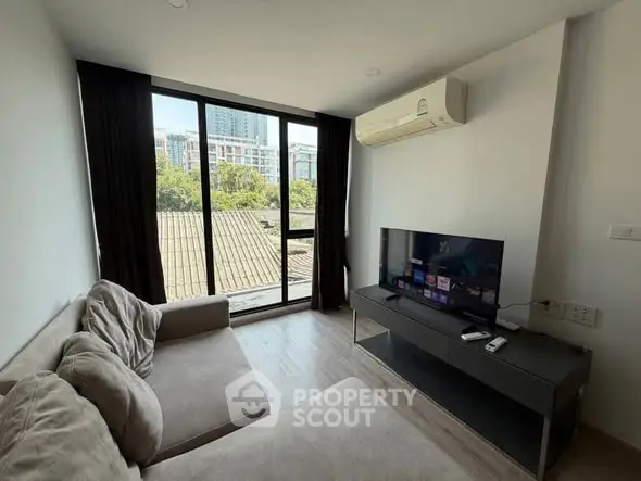 Modern living room with large window and city view, featuring a cozy sofa and flat-screen TV.