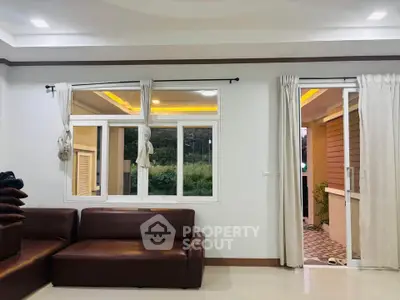Spacious living room with modern brown sofas and large windows overlooking greenery.