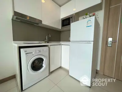 Modern compact kitchen with washing machine, fridge, and microwave in sleek white cabinetry.