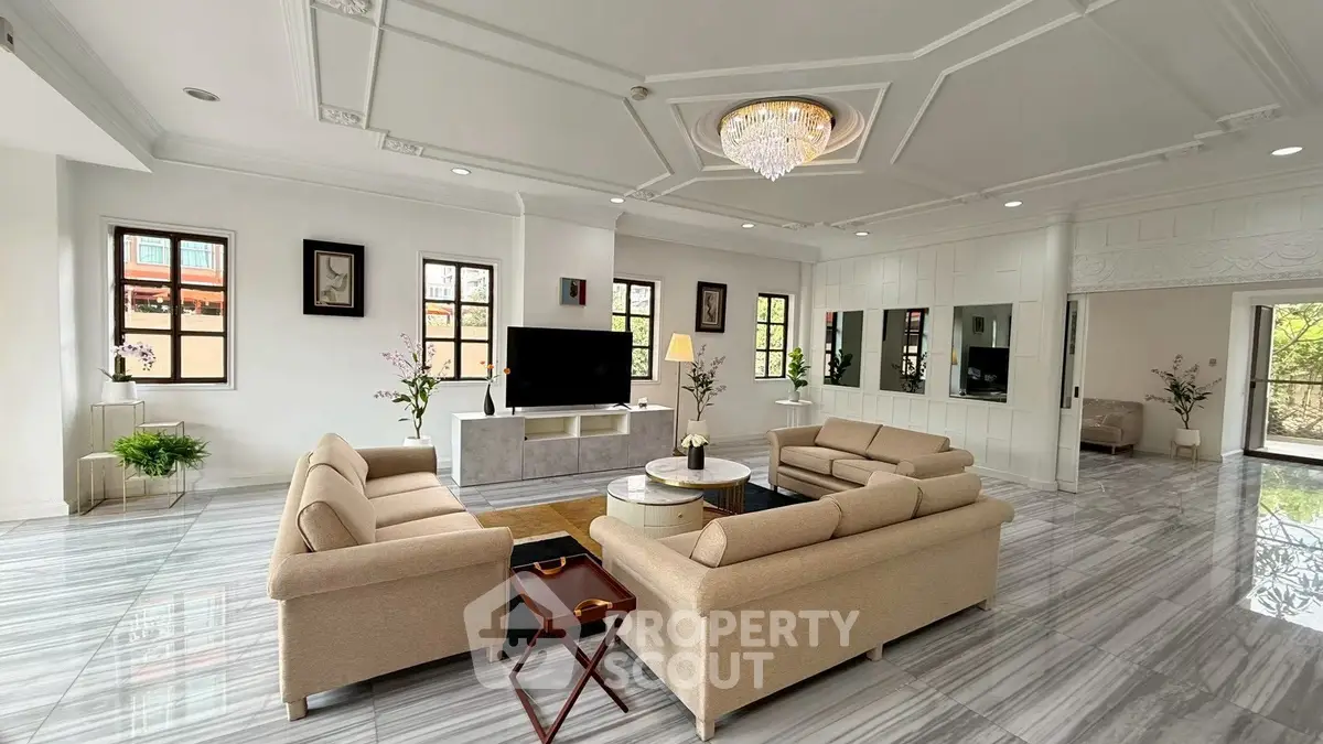 Luxurious living room with elegant chandelier and modern decor, featuring spacious seating and large windows.