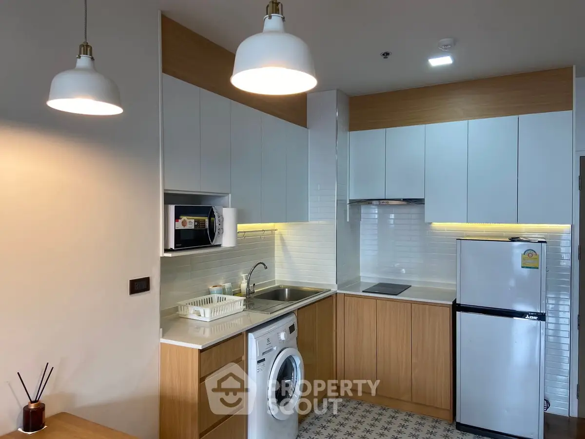 Modern kitchen with washing machine and microwave, featuring sleek cabinetry and stylish lighting.