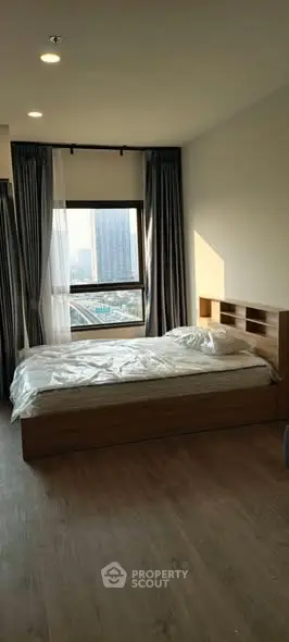 Modern bedroom with large window offering city view, featuring a cozy bed and elegant curtains.