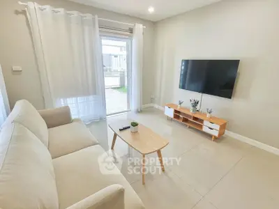Modern living room with sleek TV setup and cozy beige sofa, bright natural light from large window.