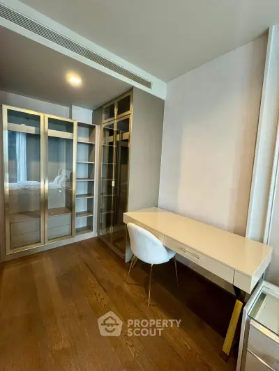 Modern study room with sleek desk and glass-door storage in a stylish apartment.