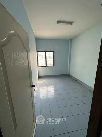 Spacious empty room with blue tiled floor and natural light from window.