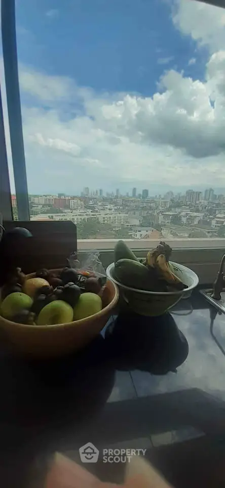 Stunning cityscape view from a high-rise apartment window with fruit bowls on the table.