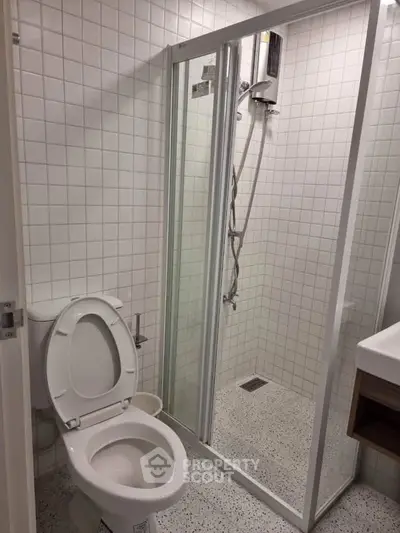 Modern bathroom with glass shower enclosure and white tiled walls.