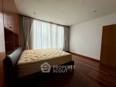 Spacious bedroom with large window and wooden flooring in modern apartment.