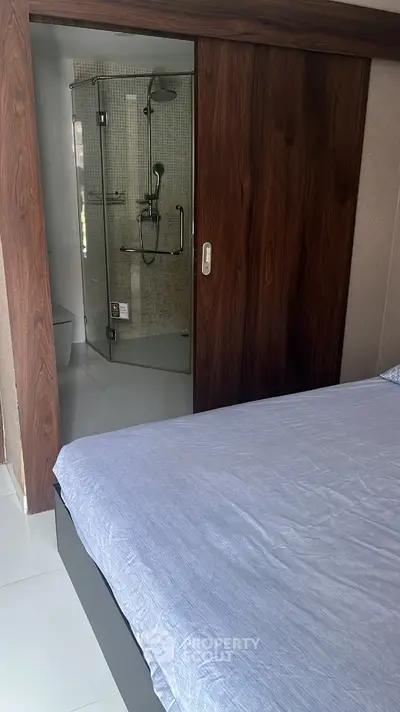 Modern bedroom with ensuite bathroom featuring sleek sliding wooden door and contemporary shower design.