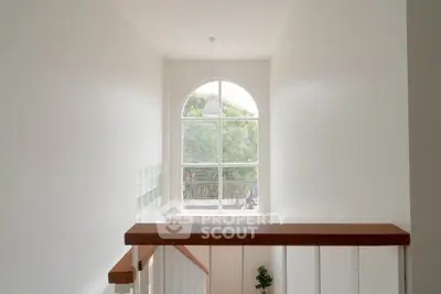 Bright stairway with large arched window and wooden railing in modern home
