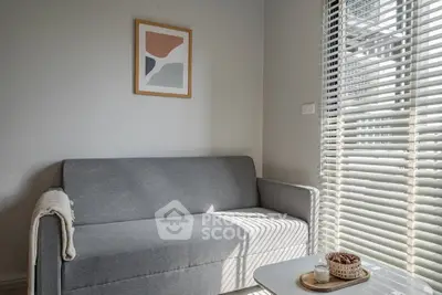 Cozy living room with modern gray sofa and abstract art, bathed in natural light through blinds.