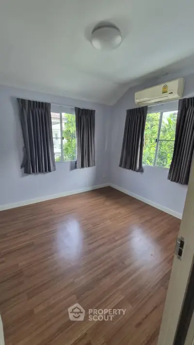 Spacious bedroom with hardwood floors and large windows offering natural light and garden views.