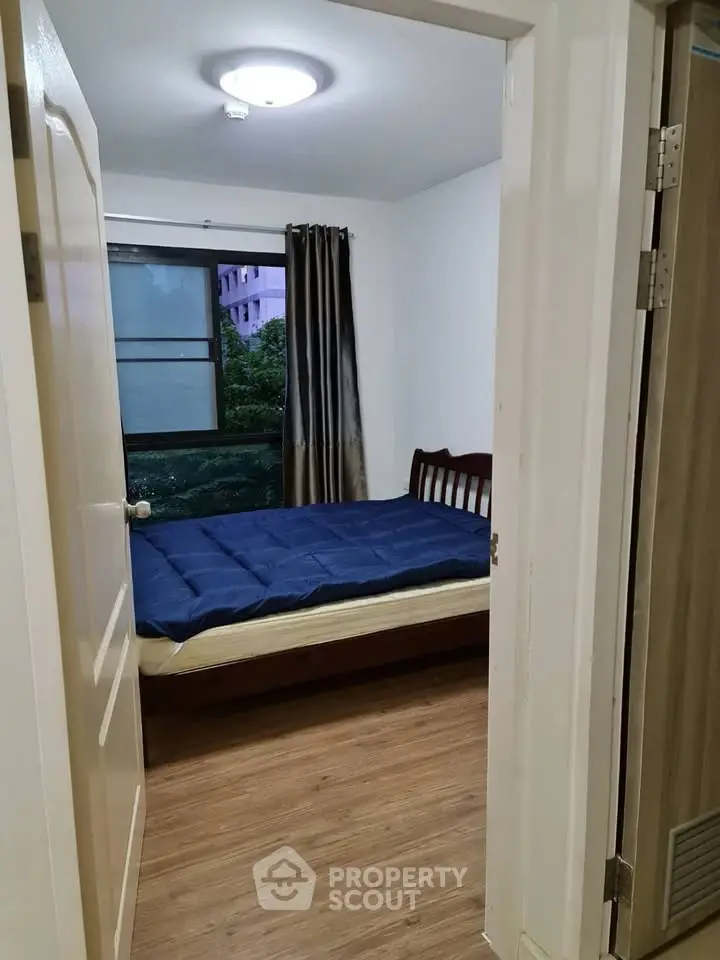 Cozy bedroom with wooden flooring and large window offering natural light.