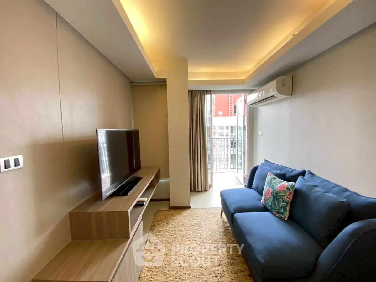 Modern living room with cozy blue sofa and flat-screen TV, featuring elegant lighting and balcony access.