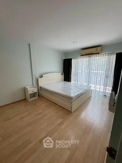 Spacious bedroom with large window and wooden flooring in modern apartment