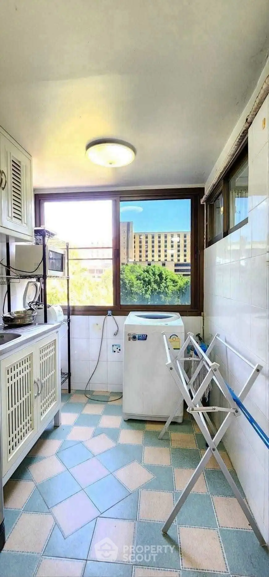 Bright kitchen with large window, washing machine, and tiled floor in modern apartment.