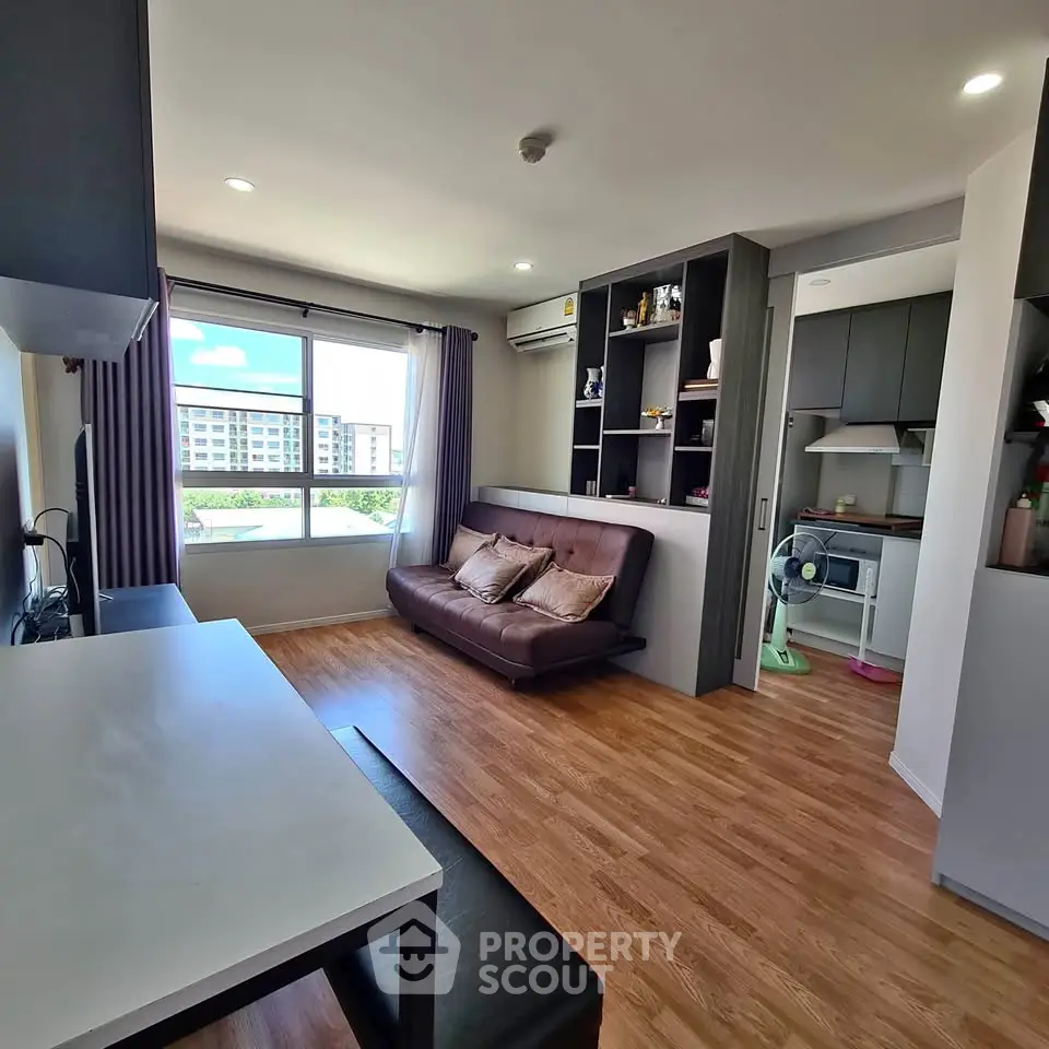 Modern living room with open kitchen, wooden flooring, and large window with city view.