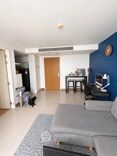 Modern living room with stylish gray sofa and blue accent wall, featuring a cozy workspace and dining area.