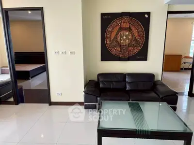 Modern living room with black leather sofa and glass coffee table, adjacent to bedroom.