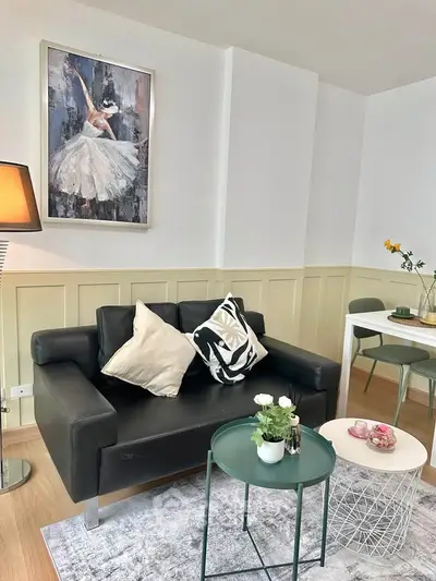 Chic living room with modern decor, featuring a stylish black sofa, elegant artwork, and cozy dining area.