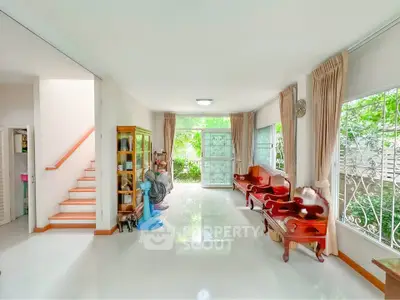 Spacious living room with elegant wooden furniture and large windows overlooking lush greenery.