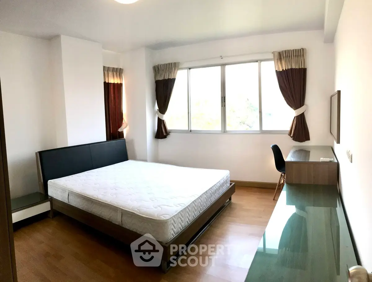 Spacious bedroom with large window and modern furnishings in a well-lit apartment.