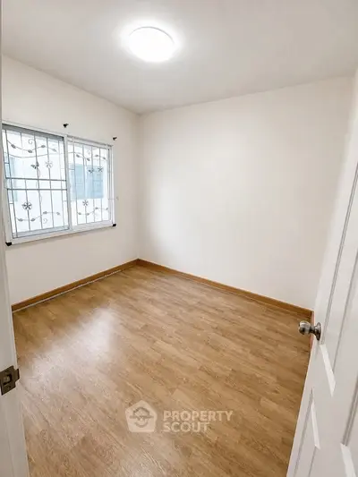Spacious empty room with wooden flooring and bright window, perfect for customization.