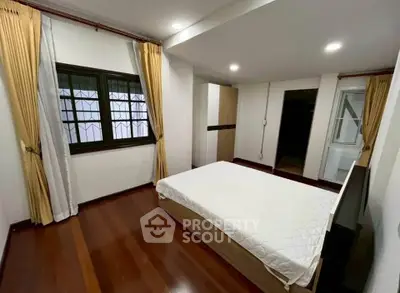 Spacious bedroom with wooden flooring and large window, perfect for relaxation.
