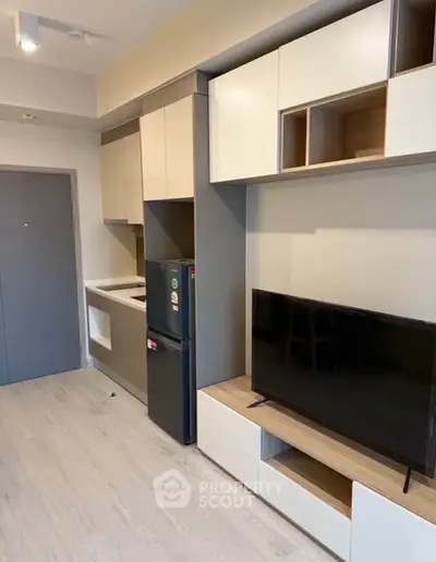 Modern compact kitchen and living area with sleek cabinetry and flat-screen TV.