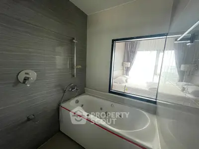Luxurious bathroom with modern jacuzzi tub and large window overlooking a bright bedroom.