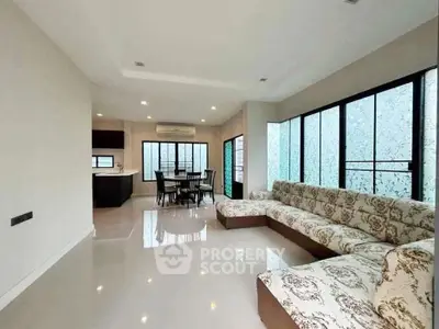 Spacious modern living room with elegant sectional sofa and dining area, featuring large windows and sleek flooring.