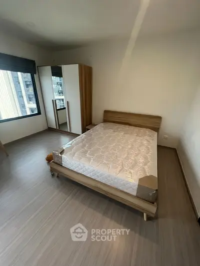 Spacious bedroom with modern wooden furniture and large window view.
