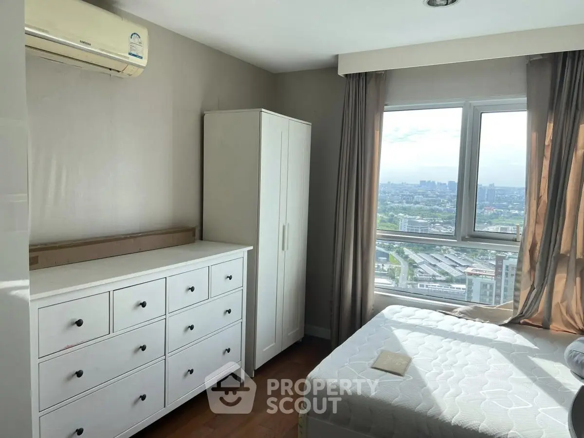 Bright bedroom with city view, featuring white furniture and large window.