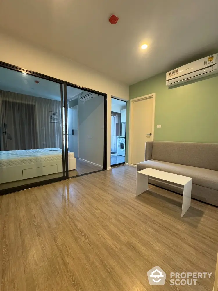 Modern apartment interior with wooden flooring and glass partition, featuring a cozy living area and bedroom.