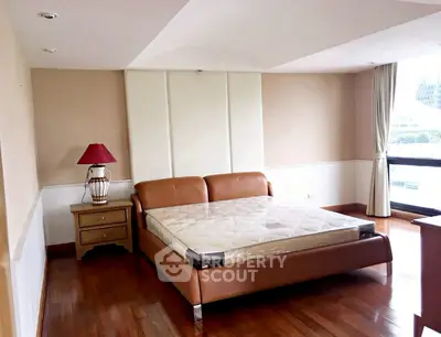 Spacious bedroom with elegant wooden flooring and large window offering natural light.