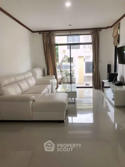 Spacious living room with white leather sofa and glass coffee table, featuring large windows for natural light.